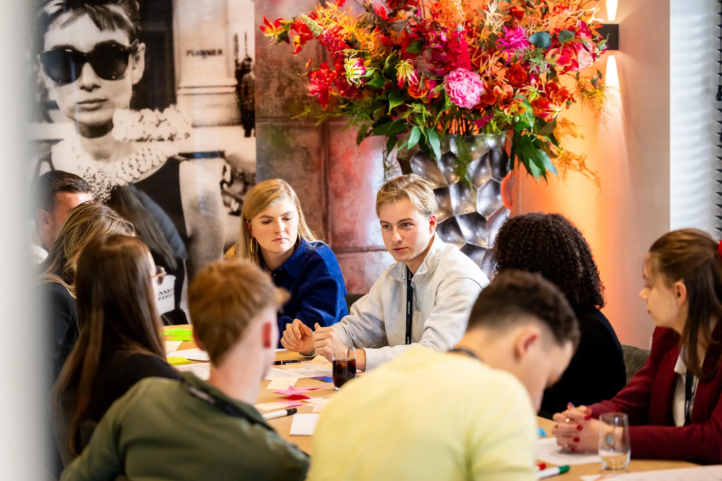 Een bijeenkomst in de wijnbar waar gasten deelnemen aan een zakelijke workshop rond een tafel met papier en stiften.