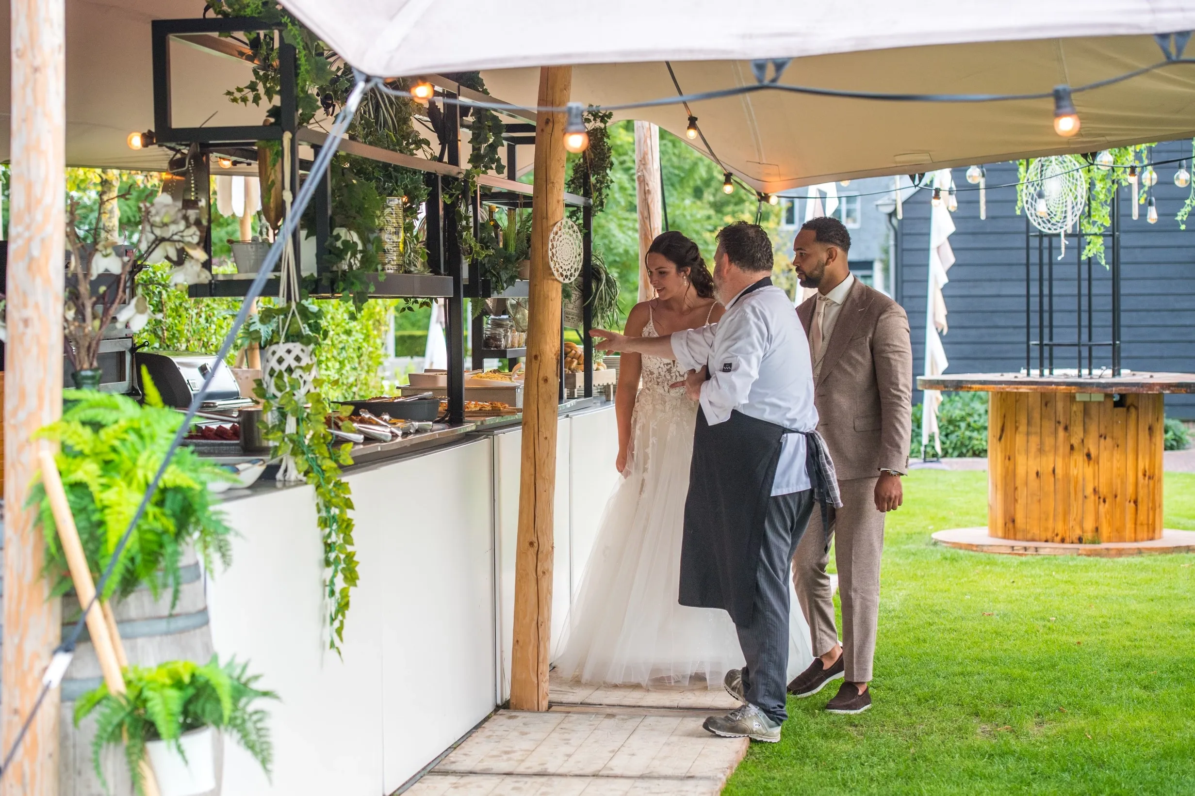 Een bruid en echtgenoot krijgen uitleg over de catering van een medewerker van Green Village, die bij een buffetopstelling in de tuin de catering heeft voorbereid.