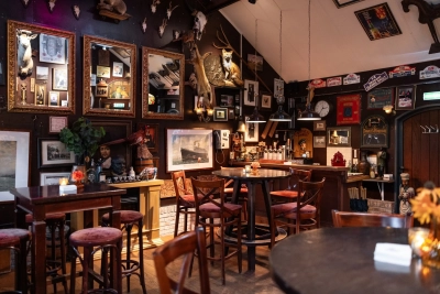 Een knusse, met hout beklede hoek van het Koetshuis met donker houten interieur, een houten vloer, rustieke houten balken en schilderijen en geweien als decoratie aan de muur.